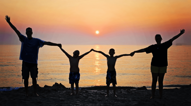 Family practicing social distancing on a beach at sunset